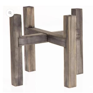 May include: A wooden plant stand with a gray wash finish. The stand has four vertical legs and a cross-beam design to support a plant pot. The wood grain is visible, adding texture to the piece. The stand is designed for indoor or outdoor use.