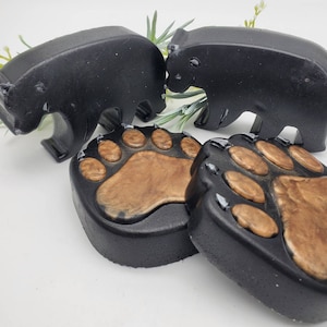 May include: Three black bear-shaped soaps and two brown paw print soaps. The bear soaps are in a standing position and the paw print soaps are lying flat.