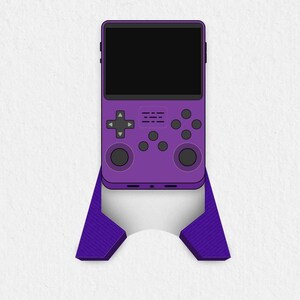 以下が含まれることがあります： 黒い画面と紫色のコントローラーが付いた紫色の携帯ゲーム機。コンソールは紫色のスタンドの上に置かれています。