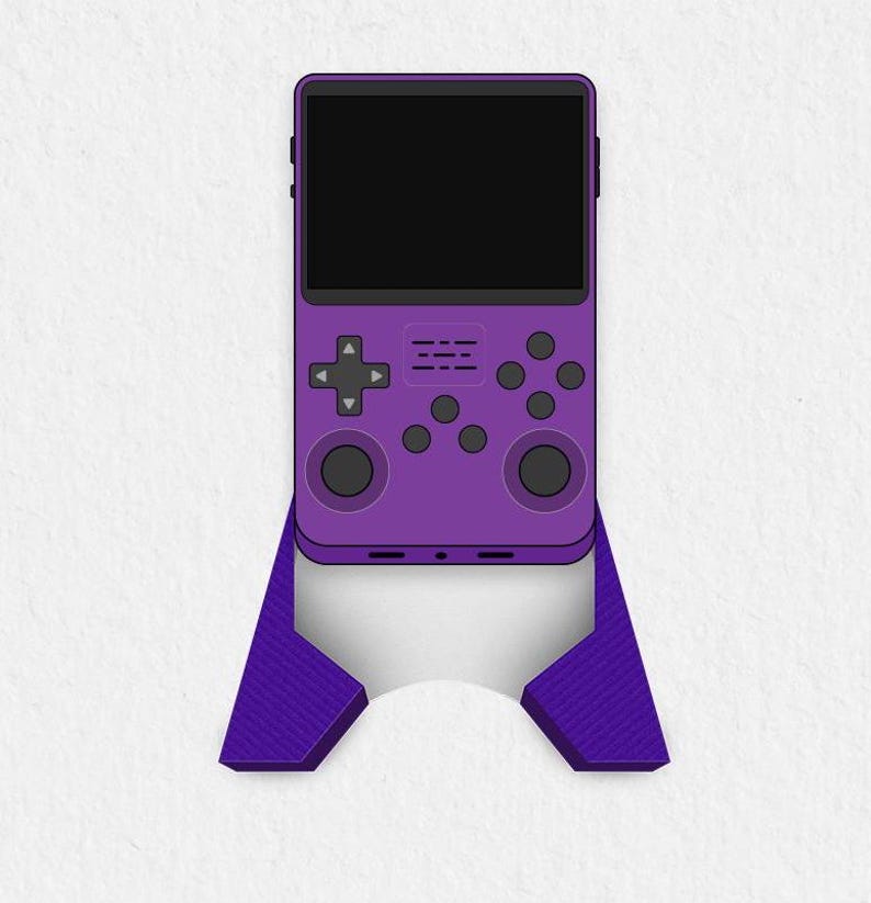 以下が含まれることがあります： 黒い画面と紫色のコントローラーが付いた紫色の携帯ゲーム機。コンソールは紫色のスタンドの上に置かれています。