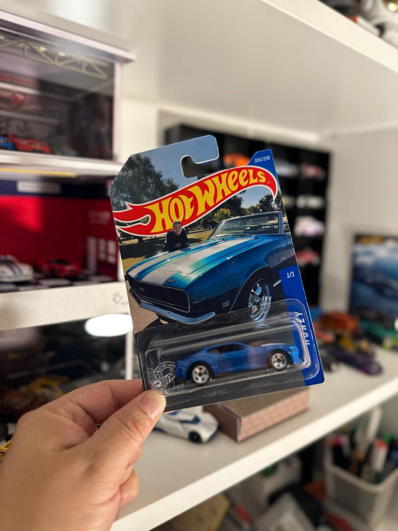 May include: A blue Hot Wheels die-cast model car in its original packaging. The packaging features a picture of a blue and white classic car. The car is a 1/1 scale model.