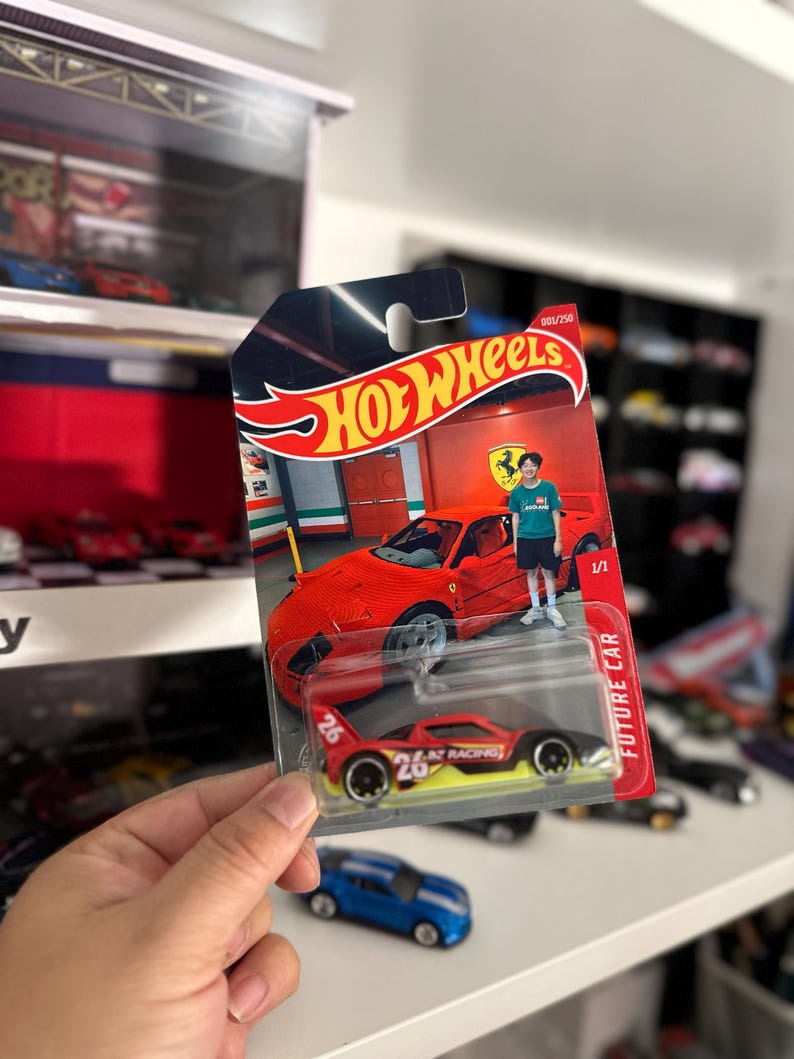 May include: A Hot Wheels die-cast toy car in a blister pack. The packaging features a red Ferrari and the Hot Wheels logo. The toy car is red, black, and yellow with the number 26. The words "FUTURE CAR" are printed on the side.