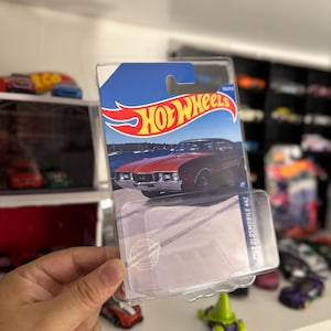 May include: A Hot Wheels die-cast car package featuring a red 1968 Oldsmobile 442. The package has a blue and white background with the Hot Wheels logo. The car is visible through the clear plastic.