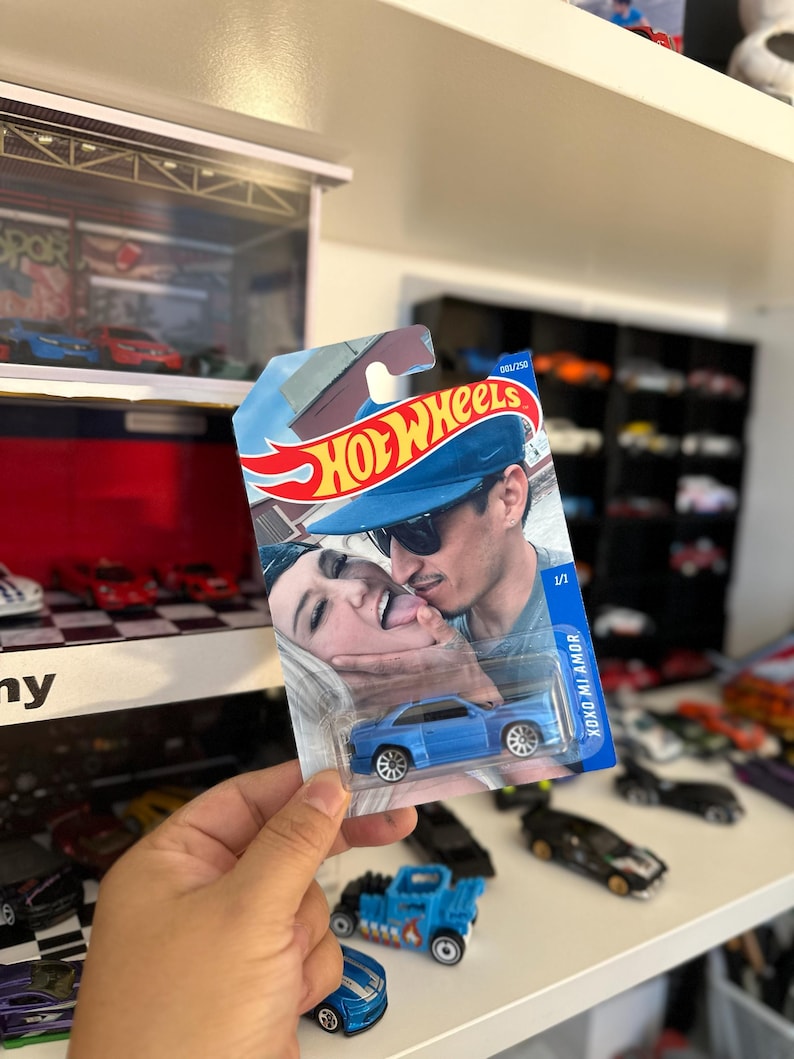 May include: A blue Hot Wheels die-cast car in its original packaging. The packaging features a photo of a couple and the text "XOXO MI AMOR". The car is a coupe with silver wheels.