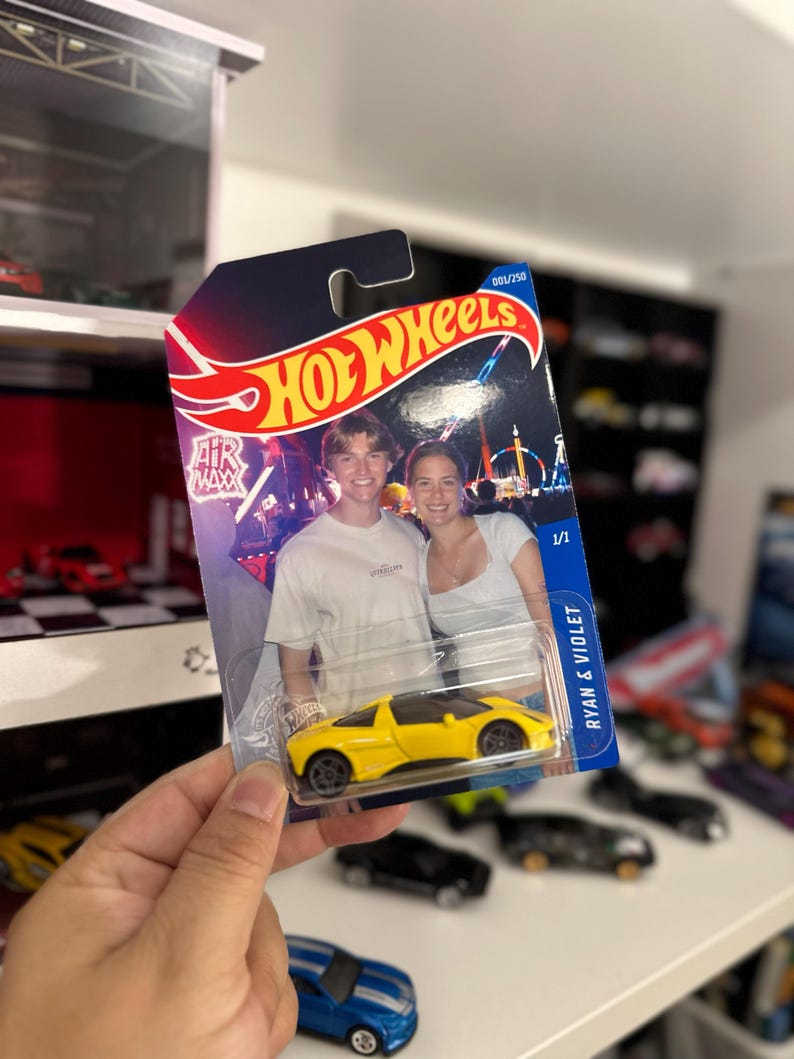 May include: A yellow Hot Wheels toy car in its original packaging. The packaging features a photo of a couple and the text "HOT WHEELS" in red and yellow. The card reads "RYAN & VIOLET".