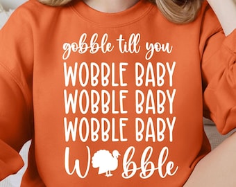 May include: Orange sweatshirt with the text "gobble til you wobble baby wobble baby wobble baby wobble" and a white turkey graphic.