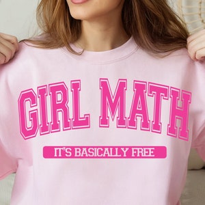 Könnte beinhalten: Rosafarbener Pullover mit dem Text "Girl Math" in rosa Schrift und dem Text "It's basically free" in kleinerer Schrift darunter.