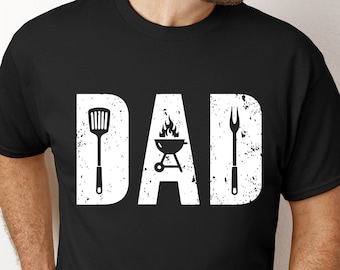 May include: Black t-shirt with a white distressed graphic that says "DAD" with a grill, spatula, and fork.