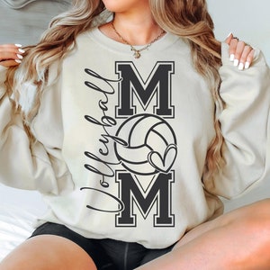 May include: A cream-colored sweatshirt with the words "Volleyball Mom" and a volleyball with a heart design printed on the front.