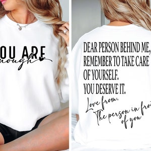 May include: White sweatshirt with the text "YOU ARE enough" on the front and the text "DEAR PERSON BEHIND ME, REMEMBER TO TAKE CARE OF YOURSELF. YOU DESERVE IT. Love from. The person in front of you" on the back.