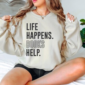 May include: A cream-colored sweatshirt with the text "LIFE HAPPENS. BOOKS HELP." printed in black.