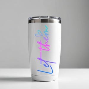 May include: White travel tumbler with a silver lid. The tumbler features the words "Let them" in a gradient of blue, purple, and pink, with a small heart symbol above the word "them".