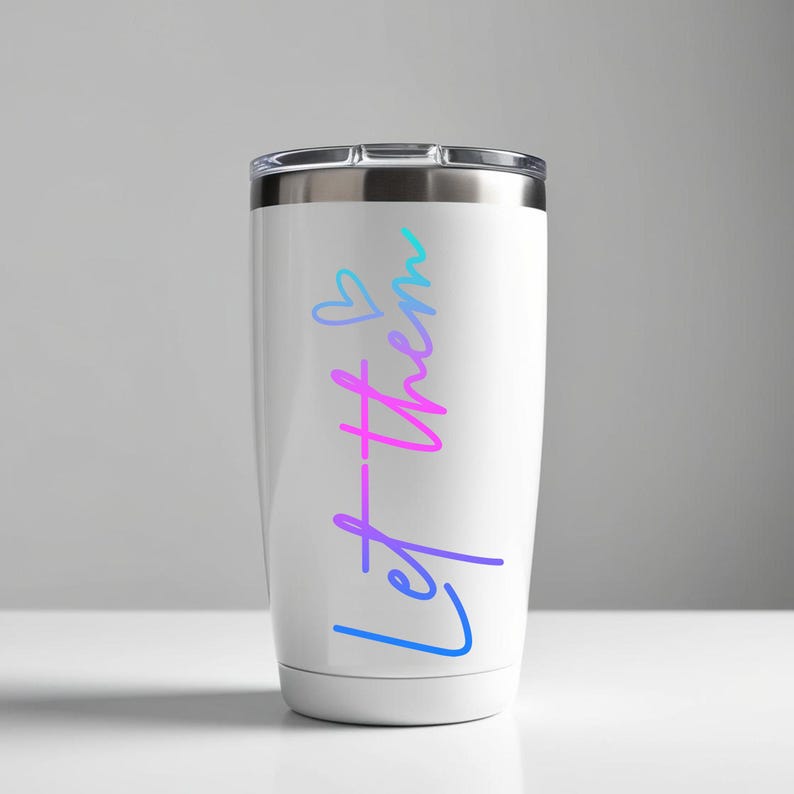 May include: White travel tumbler with a silver lid. The tumbler features the words "Let them" in a gradient of blue, purple, and pink, with a small heart symbol above the word "them".