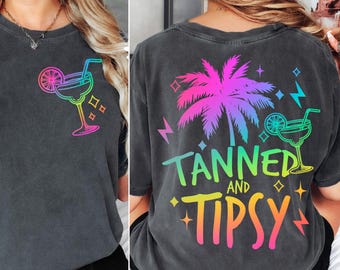 May include: A black t-shirt with a rainbow gradient design featuring a palm tree, a cocktail glass, and the text "Tanned and Tipsy".