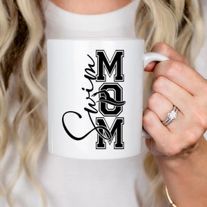 May include: White ceramic mug with a black design that says "Swim Mom" in a stylized font.