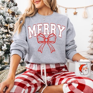 May include: A grey sweatshirt with the word "MERRY" in white letters and a red bow. The sweatshirt is being worn by a person wearing red and white checked trousers.