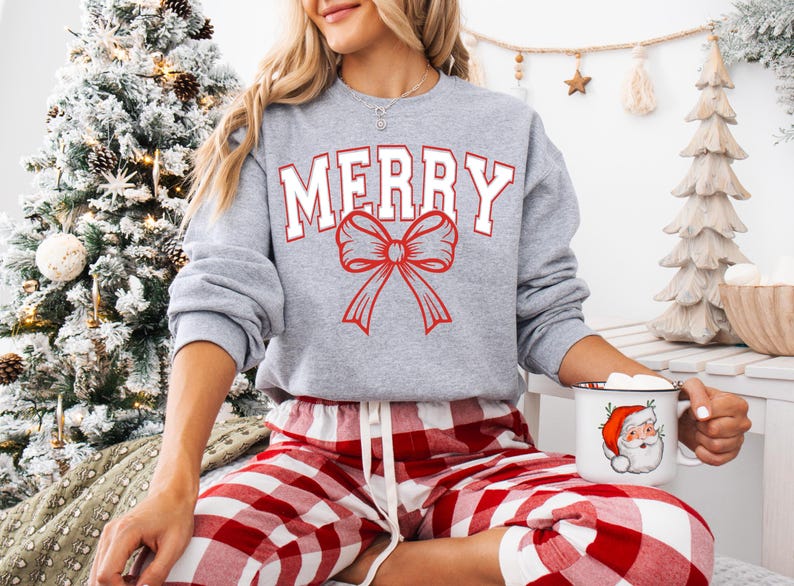 May include: A grey sweatshirt with the word "MERRY" in white letters and a red bow. The sweatshirt is being worn by a person wearing red and white checked trousers.