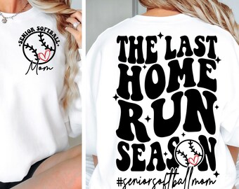 以下が含まれることがあります： 白いスウェットシャツに、黒い文字で「The Last Home Run Season #seniorsoftballmom」と書かれています。テキストの中に、赤いハートの付いたソフトボールがあります。