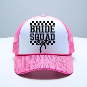 Puede incluir: Gorra de camionero rosa y blanca con el texto "BRIDE SQUAD" en letras negras. La gorra tiene una parte trasera de malla rosa y un panel frontal blanco con un lazo negro.