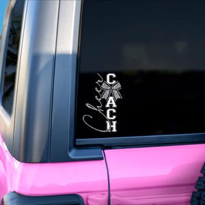 May include: A pink Jeep with a black window featuring a white and silver glitter "Cheer Coach" decal. The decal includes a bow and the word "Coach" vertically. The background shows a beach and palm trees.