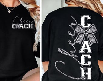Puede incluir: Sudadera negra con la inscripción "Cheer Coach" en blanco y purpurina plateada. El diseño frontal presenta el texto y un lazo. La parte trasera de la camiseta tiene la palabra "Cheer" en cursiva y la palabra "Coach" en letras de bloque con un lazo.