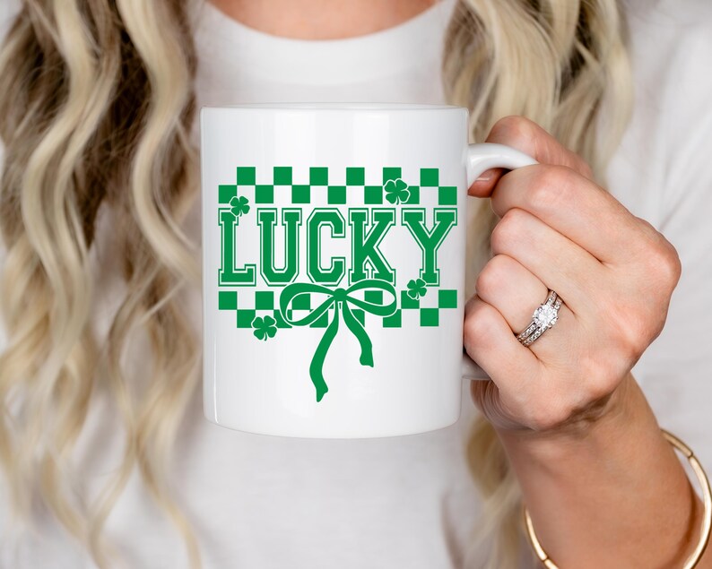 Pu&ograve; includere: Una tazza in ceramica bianca con un motivo a scacchi verdi e un fiocco verde. La parola "LUCKY" &egrave; scritta in lettere verdi sulla tazza.