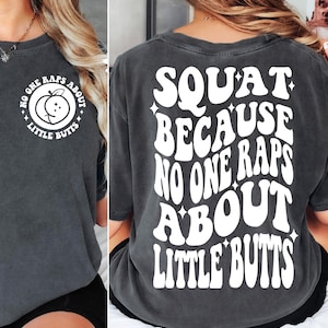 Op de afbeelding: Donkergrijs t-shirt met witte tekst. De voorkant van het shirt heeft een afbeelding van een perzik met de tekst "NO ONE RAPS ABOUT LITTLE BUTTS". De achterkant van het shirt zegt "SQUAT BECAUSE NO ONE RAPS ABOUT LITTLE BUTTS".