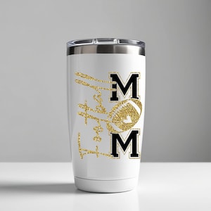 May include: White tumbler with a silver lid featuring a gold glitter football and the word "MOM" in black block letters. The words "Love Football" are in gold glitter script.