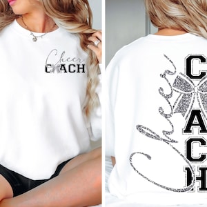 May include: White sweatshirt with "Cheer Coach" text in black and silver glitter. The front features the text "Cheer Coach" with a bow graphic. The back has a large bow graphic and the word "Coach" vertically.