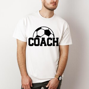 May include: White t-shirt with a black soccer ball graphic and the word "COACH" printed in black.