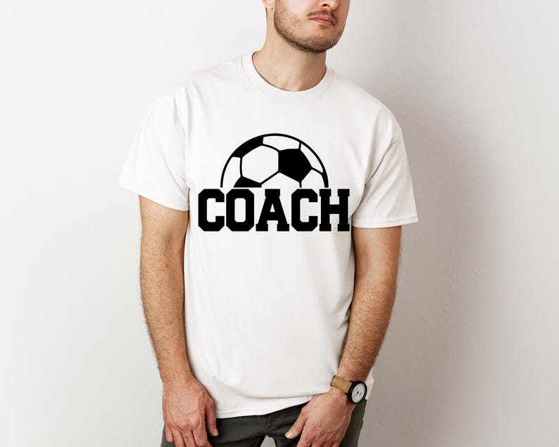 May include: White t-shirt with a black soccer ball graphic and the word "COACH" printed in black.