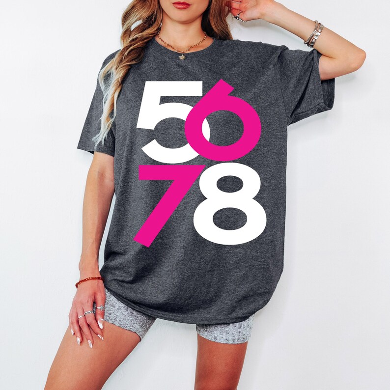 May include: A dark gray oversized t-shirt with a graphic design of the numbers 5678. The numbers are in white and pink.
