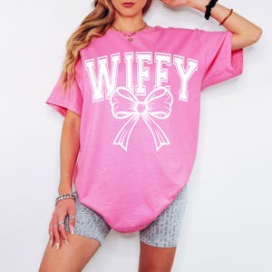 May include: Pink oversized t-shirt with the text "WIFFY" in white with a white bow underneath.