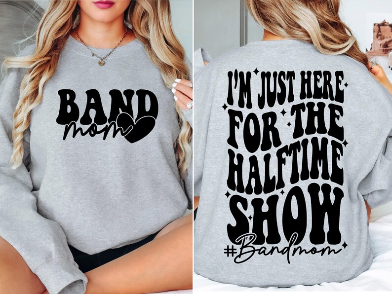 Puede incluir: Sudadera gris con el texto "Band Mom" y un coraz&oacute;n en la parte delantera. La parte posterior de la sudadera tiene el texto "I'm just here for the halftime show #Bandmom" en una fuente retro.