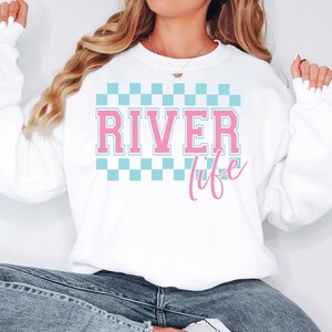 May include: White sweatshirt with a blue and white checkered pattern and the text "RIVER life" in pink.