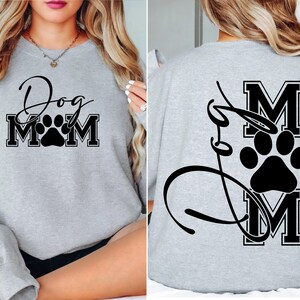 Puede incluir: Sudadera gris con texto negro que dice "Dog Mom" con una huella de pata en el medio de la palabra "Mom". La parte posterior de la sudadera tiene un dise&ntilde;o negro con la palabra "Mom" en una fuente grande con una huella de pata en el medio.
