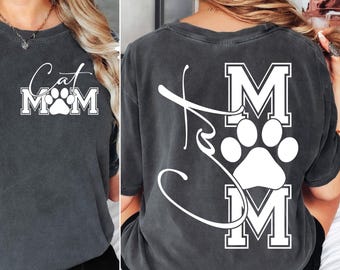 May include: Dark gray t-shirt with the words "Cat Mom" in a white script and block letters, with a paw print in the center. The back of the shirt also features the words "Cat Mom" in a similar design.