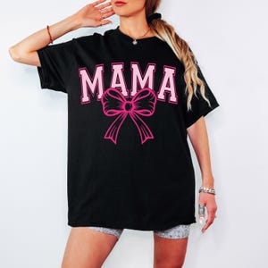 May include: Black oversized t-shirt with the word "MAMA" in pink letters and a pink bow.