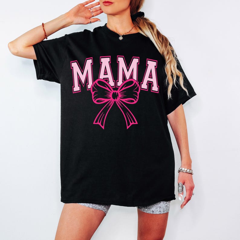 May include: Black oversized t-shirt with the word "MAMA" in pink letters and a pink bow.