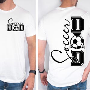 Peut inclure: T-shirt blanc avec un texte noir qui dit "Soccer Dad" sur le devant et "Soccer Dad" avec un ballon de football au milieu sur le dos.