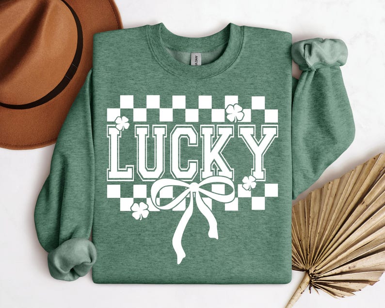 Pu&ograve; includere: Felpa verde con un motivo a scacchi bianchi, un fiocco bianco e la parola "LUCKY" in lettere bianche.