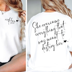Op de afbeelding: Wit sweatshirt met de tekst "She overcame everything that was meant to destroy her" op de achterkant en "Powerful" met een hartje op de voorkant.