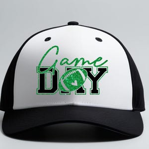 K&ouml;nnte beinhalten: Eine schwarz-wei&szlig;e Baseballkappe mit dem Schriftzug "Game Day" in gr&uuml;nem Glitzer-Schriftzug und Blockbuchstaben. Das "O" in "Day" ist durch einen gr&uuml;nen Glitzer-Football ersetzt. Die Kappe hat einen gebogenen Schirm.