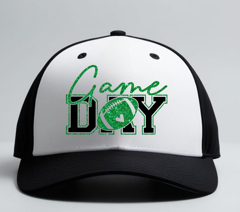 K&ouml;nnte beinhalten: Eine schwarz-wei&szlig;e Baseballkappe mit dem Schriftzug "Game Day" in gr&uuml;nem Glitzer-Schriftzug und Blockbuchstaben. Das "O" in "Day" ist durch einen gr&uuml;nen Glitzer-Football ersetzt. Die Kappe hat einen gebogenen Schirm.