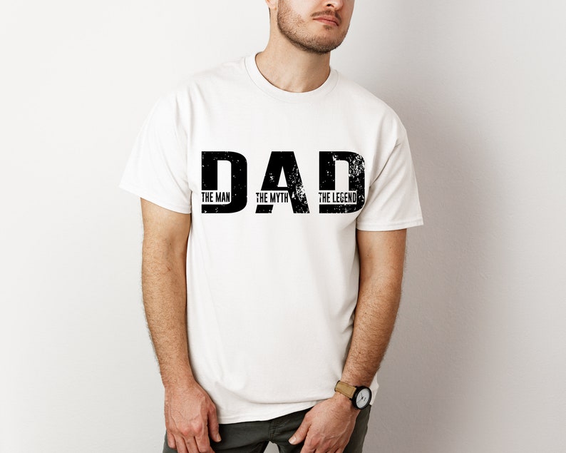K&ouml;nnte beinhalten: Ein wei&szlig;es T-Shirt mit kurzen &Auml;rmeln und dem schwarzen, im Used-Look gestalteten Schriftzug DAD in gro&szlig;en Druckbuchstaben. Unter jedem Buchstaben steht in kleinerer schwarzer Schrift THE MAN, THE MYTH und THE LEGEND als Grafik.