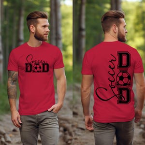 Peut inclure: T-shirt rouge avec un texte noir qui dit "Soccer Dad" et un graphique de ballon de football sur le devant. Le dos du t-shirt a le texte "Soccer Dad" verticalement avec un graphique de ballon de football.