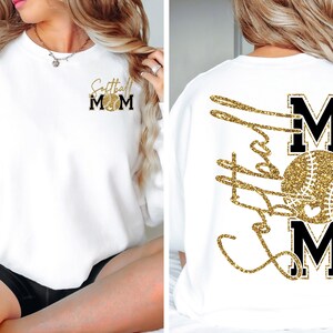 May include: White sweatshirt with gold glitter text and a softball design. The front features "Softball Mom" with a softball graphic. The back displays "Softball Mom" with a softball graphic. A comfortable, casual top for softball enthusiasts.