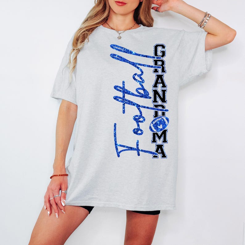 Pu&ograve; includere: T-shirt grigio chiaro con le parole "Football Grandma" in glitter blu. La parola "Grandma" &egrave; impilata verticalmente in bianco e nero con una grafica di football.