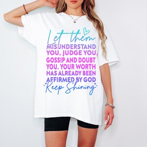 May include: White t-shirt with a teal and purple graphic that reads "Let them misunderstand you, judge you, gossip and doubt you. Your worth has already been affirmed by God. Keep Shining."
