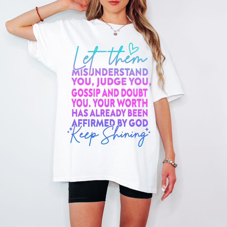 May include: White t-shirt with a teal and purple graphic that reads "Let them misunderstand you, judge you, gossip and doubt you. Your worth has already been affirmed by God. Keep Shining."